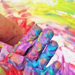A photograph of a hand covered in many colours of paint