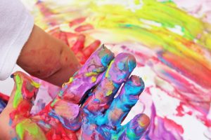 A photograph of a hand covered in many colours of paint