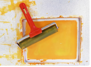 A printmaking roller in a tray of yellow paint