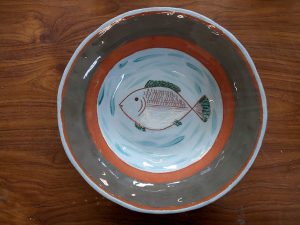 A grey and orange ceramic plate with a picture of a fish in the centre