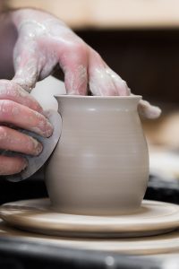 Hands polishing a ceramic pot on a potters wheel