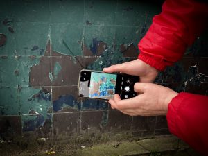 Close up photograph of hands holding smartphone taking a picture of a wall of tiles with peeled paint 