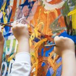 Young people's hands painting cplours on a wall with paintbrushes