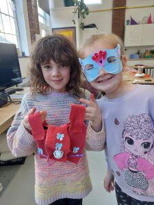 2 girls showing off craft work. One girl wears blue mask