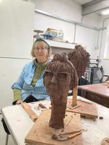 Sculpture student sitting with a sculpyure of her head on the table