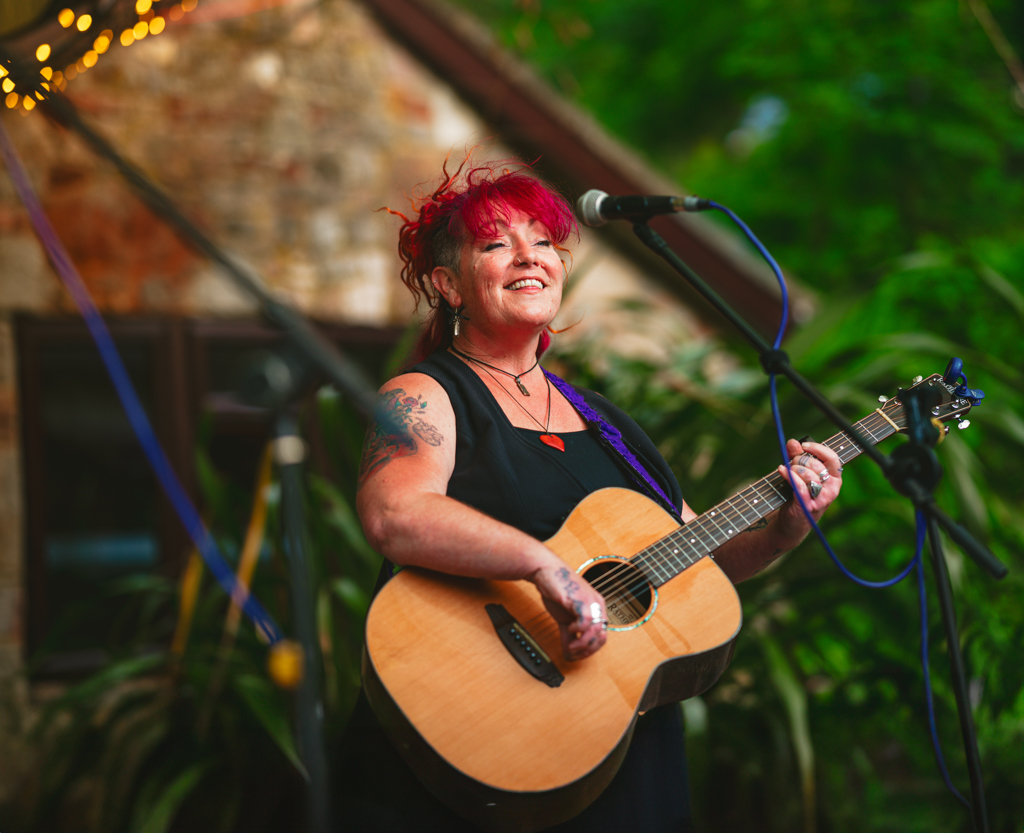 woman with red hair singing playing acoustic guitar