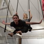 Young aerial student swinging on trapeze with arms out wide.