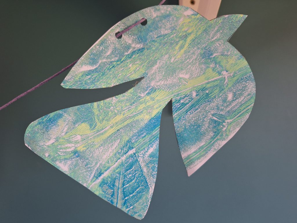 A cut-out bird shape with a printed, marbled pattern in shades of blue, green, and white, created using gelli printing.